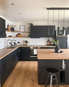 a kitchen with wooden floors and black cabinets is pictured in this image, there are two stools at the center of the island