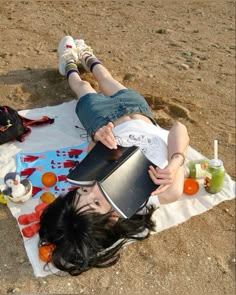 a woman laying on top of a towel with a bucket in her hand and other items around her