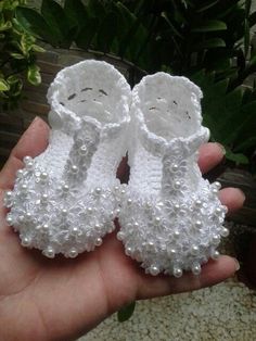 someone is holding two baby shoes made out of crocheted yarn and pearl beads