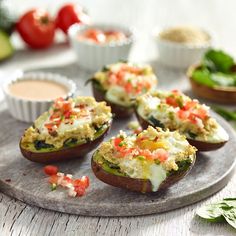 several stuffed avocados on a plate with dipping sauces and fresh basil leaves