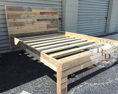 a bed frame made out of wood sitting on top of a parking lot next to a building