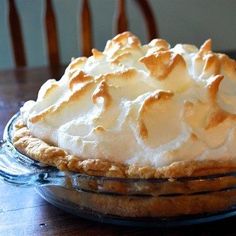 a pie sitting on top of a wooden table next to a glass bowl filled with whipped cream