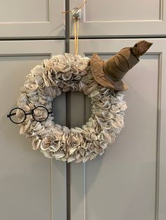 a wreath made out of old books with a hat and glasses hanging on the front door