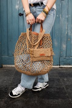 a woman is holding a straw bag in front of a blue door with her hands on the handle