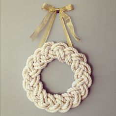 a rope wreath hanging on the wall with a ribbon around it and a gold bow