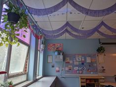 an empty classroom is decorated with purple and white ribbons hanging from the ceiling, along with potted plants