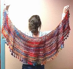 a woman is holding up a multicolored shawl