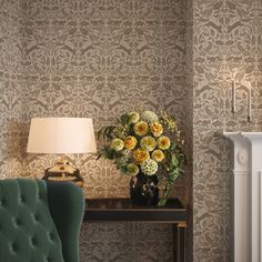 a green chair sitting in front of a table with flowers on it and a lamp next to it