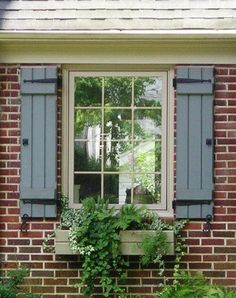 a brick house with blue shutters and green plants in the window sill next to it