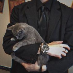 a man in a suit holding a cat with his arm wrapped around the other hand