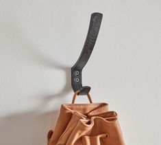 a brown purse hanging from a hook on a white wall with a black object in the corner