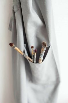 three brushes are sticking out of the pocket of a gray coat, which is partially covered by a white sheet