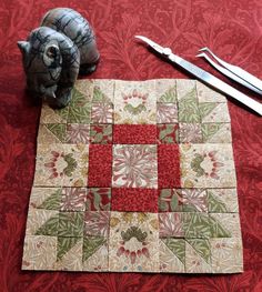 a piece of cloth and scissors are on the floor next to a quilted square