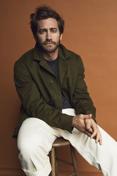 a man sitting on top of a stool wearing white pants and a green blazer