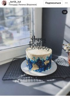 a blue and white birthday cake sitting on top of a table next to a window