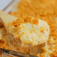 a casserole dish filled with macaroni and cheese being lifted by a wooden spoon