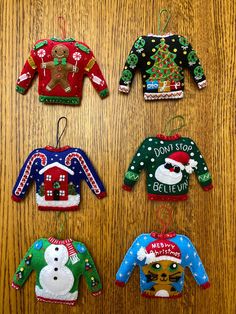 four christmas sweater ornaments hanging on a wooden table