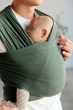 a woman holding a baby in a green wrap