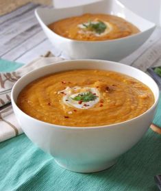 two white bowls filled with carrot soup on top of a green cloth next to silverware