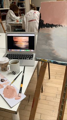 a laptop computer sitting on top of a white table next to a painting easel