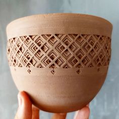 a hand holding a clay bowl with intricate designs on it