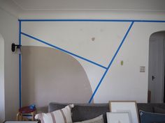 a living room with blue tape on the wall and pictures on the couch in front of it