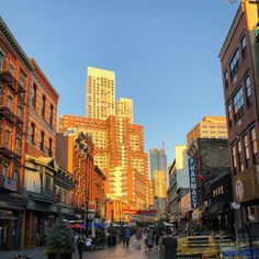 people are walking down the street in front of tall buildings and skyscrapers at sunset