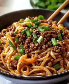 a black bowl filled with noodles and meat on top of a table next to chopsticks