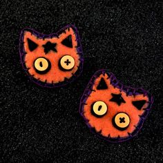 two orange and purple cat shaped buttons on black carpeted area with dark flooring