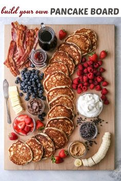 pancakes, strawberries, bananas, blueberries and other foods are arranged on a cutting board