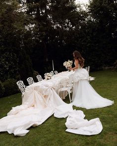 a woman sitting at a long table with white cloths on it in the grass