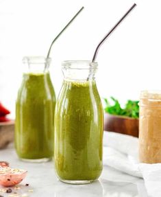 two mason jars filled with green smoothie next to some vegetables and other food items