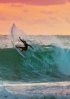 a man riding a wave on top of a surfboard in the ocean at sunset