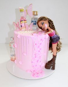 a barbie doll standing next to a pink cake with bottles on the top and decorations around it