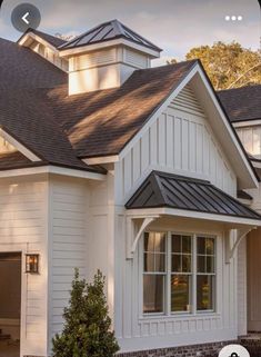 a white house with black shingles on the roof and two garages in front