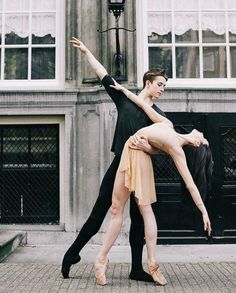 a man and woman are dancing in front of a building on the street with their arms around each other