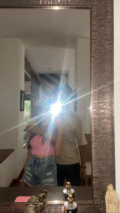 a man and woman standing in front of a mirror with the sun shining through it