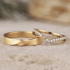 two gold wedding rings sitting on top of a stone surface with diamonds in the middle