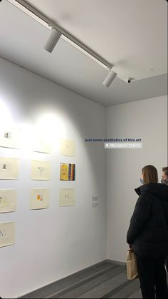 two women looking at artwork on the wall in an art gallery with white walls and grey carpet