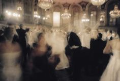 blurry photograph of people in formal wear dancing at a wedding reception with chandeliers hanging from the ceiling