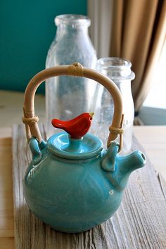 a blue teapot with a red bird on it sitting on top of a wooden table