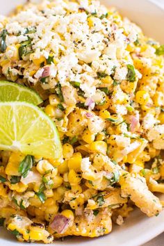 a white plate topped with corn salad next to a lime wedge