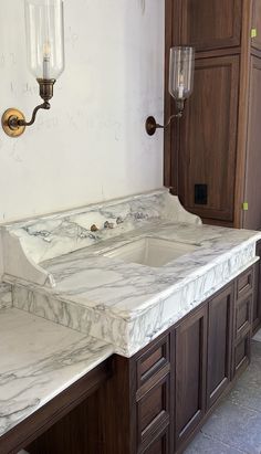 a bathroom with marble counter tops and wooden cabinets in the corner, next to a light fixture