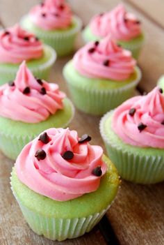 cupcakes with pink frosting and sprinkles sitting on a wooden table