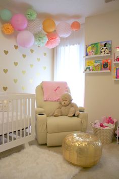 a baby's room decorated in pink, yellow and white with balloons above the crib