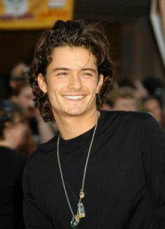 a smiling young man wearing a black t - shirt and silver necklace with green beads