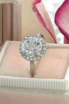 a diamond ring sitting on top of a pink velvet box next to a purple flower