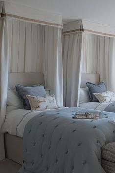 two beds in a bedroom with white curtains and blue bed linens on the covers