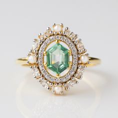 Adorned with an exquisite fern green topaz, this statement ring is set amidst a dazzling CZ and iridescent pearl halo for a radiant finish. Elegant and exclusive, this angelic design exudes class and sophistication - a must-have for any luxury jewelry lover. Luxury Green Halo Design Engagement Ring, Green Halo Engagement Ring, Luxury Gold Gemstones With Halo Setting, Unique Gemstone Ring, Angelic Design, Pearl Halo Ring, Green Engagement Rings, Pearl Halo, Vintage Wedding Rings