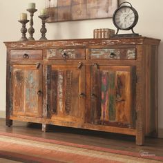 an old wooden cabinet with two candles on top and a clock in the corner next to it